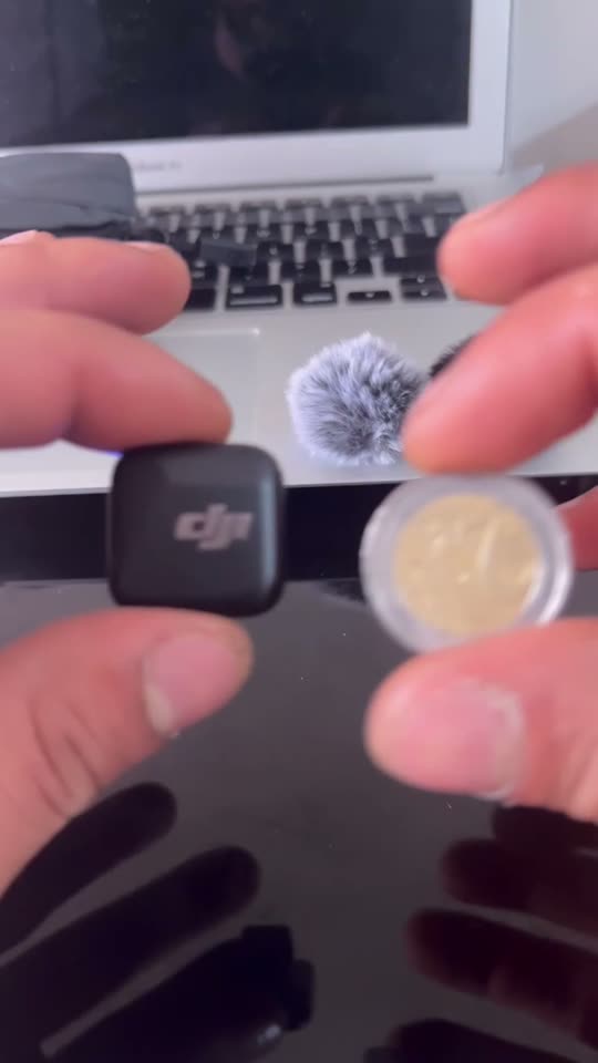 Hands holding a mini wireless microphone next to a coin