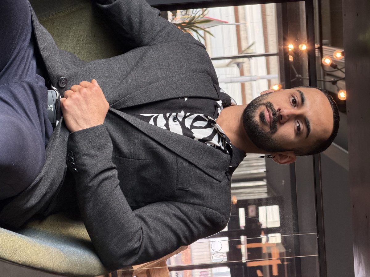 Moo in a dark blazer and patterned shirt, seated in a warmly lit lounge