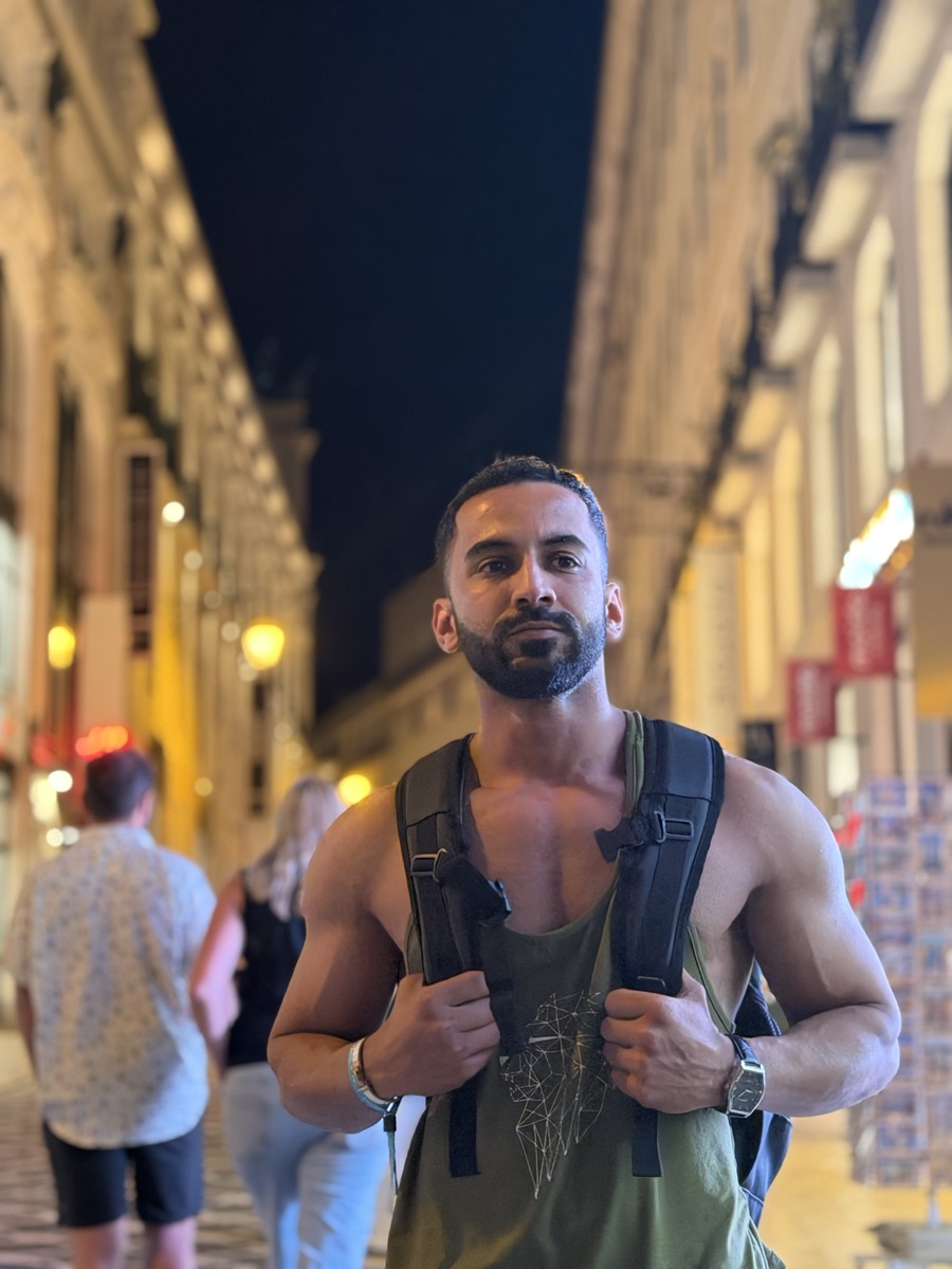 Moo in a tank top with a backpack on a lit-up city street at night